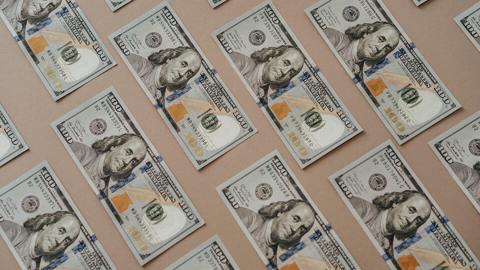 Hundred-dollar bills arranged on a pink background