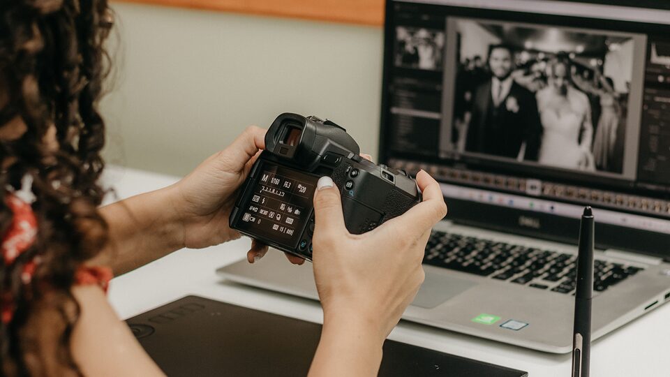Photographer reviewing images on a camera beside a laptop